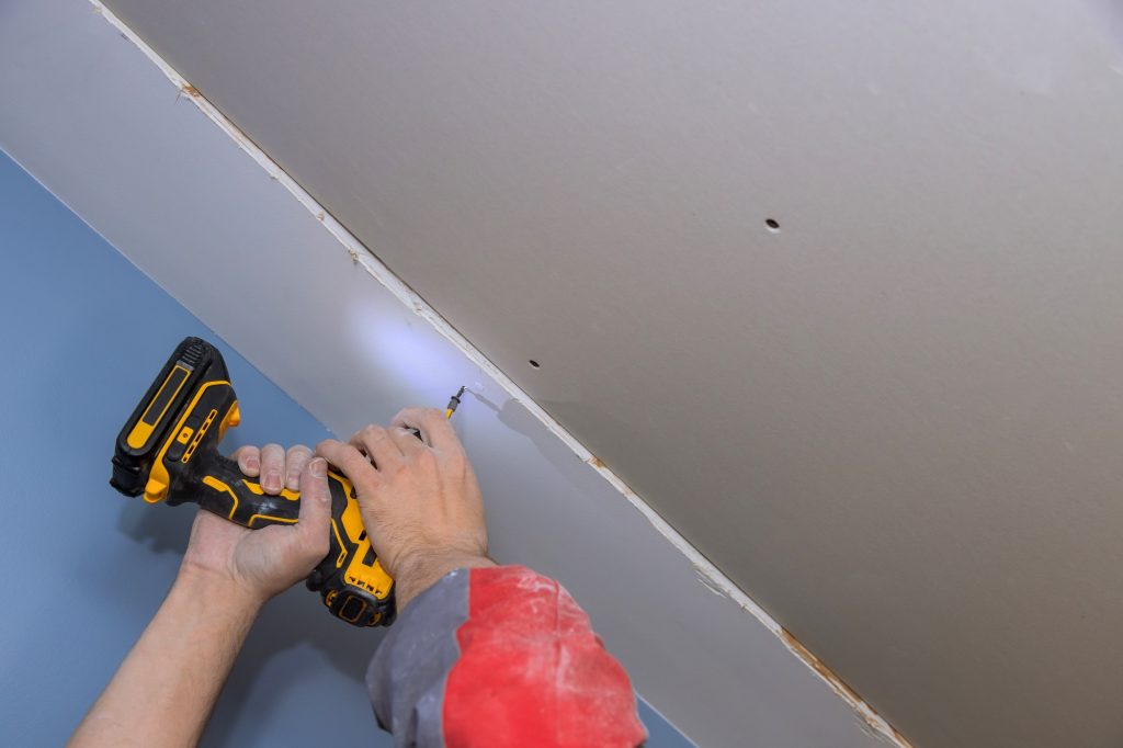 Screwing drywall to the ceiling with worker using screwdriver